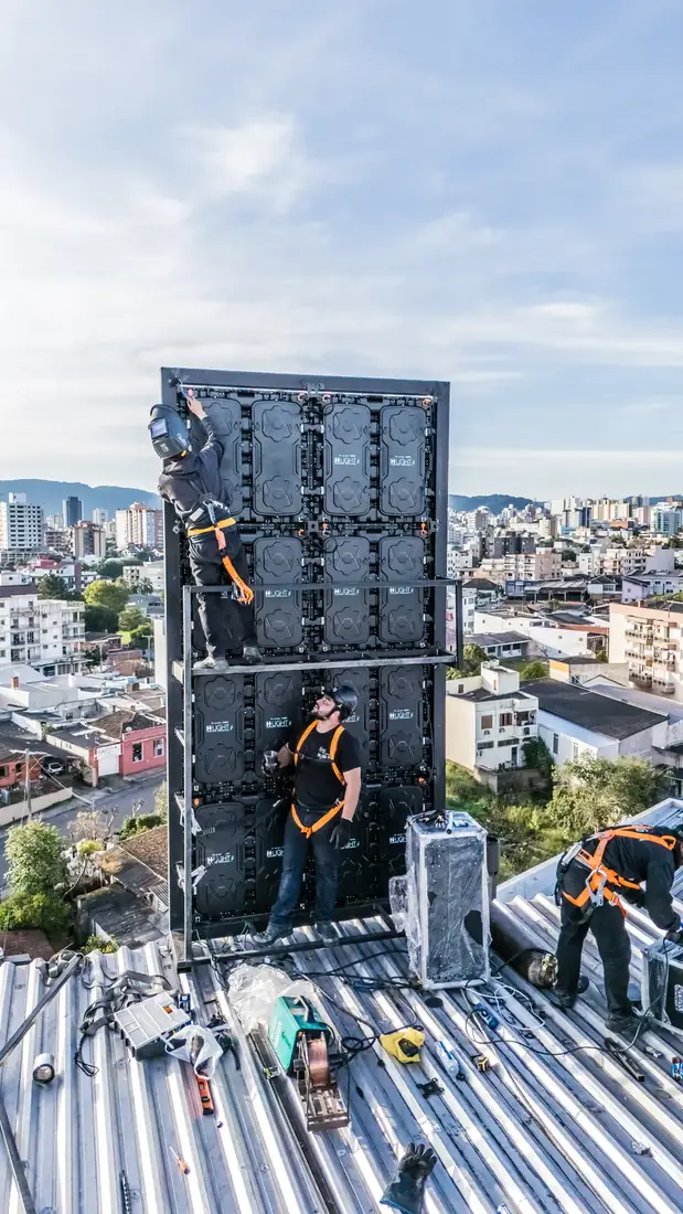 Equipe fixando estrutura de painel de LED na fachada de um prédio